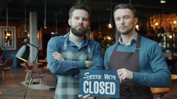 Portrait of Guys in Aprons Changing Closed To Open Sign in Modern Cafe Smiling