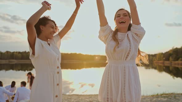 Two Female Friends Dance and Jump at a Sunset Beach Party