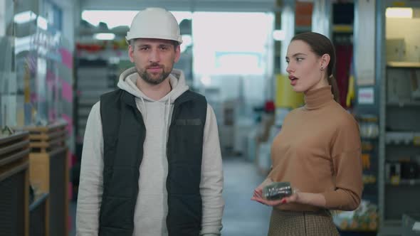 Joyful Young Woman Hitting Hammer on Hard Hat with Cheerful Man Grimacing