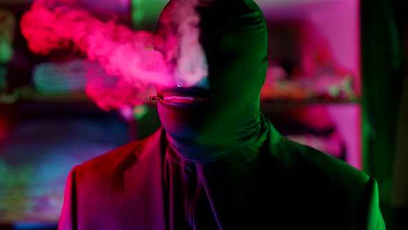 a Man in a Black Knitted Mask Without Eyes Lets Out Clouds of Smoke From Nose in a Neon Flashing