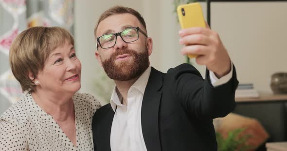 Handsome Man in Suit Doing Selfie with His Cheerful Grandmother While Visiting Her at Home, Mature