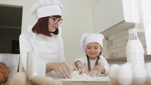 Cute Girl and Her Beautiful Mom in Hats of Chef and Apron for Cooking are Looking at Each Other
