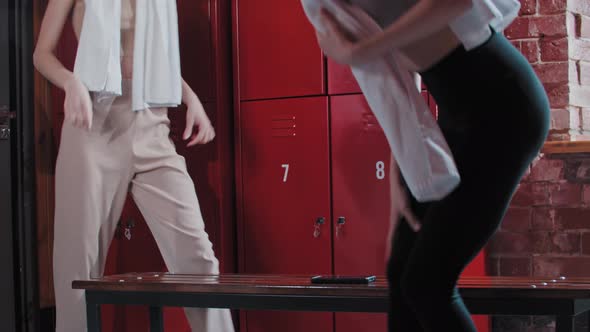 Two Young Women Sits Down on a Bench in the Locker Room After Training and Takes Off the Shoes