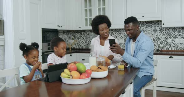 Black-Skinned Couple Reviewing Apps on Phone and their Two Small Daughters which Using Tablet PC