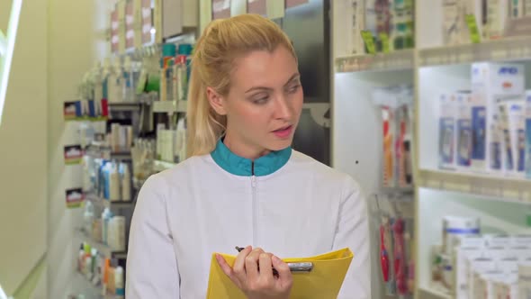 Cheerful Female Pharmacist Filling Papers, Working at the Drugstore