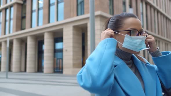 Young Businesswoman Putting on Face Mask Walking Outdoors in Street