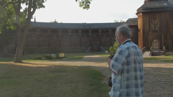 Pensioner Holds Black Camera and Takes Photo in Museum Park