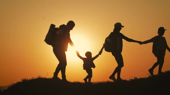 Silhouettes of Father, Mother and Children Hiking. Baby Sits on the Shoulders of His Father. Hiking