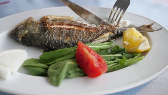 Man Is Eating Frying Fish with Fork and Knife in Restaurant, Dish Closeup.