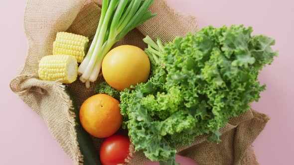 Video of fresh fruit and vegetables in rustic bag over pink background