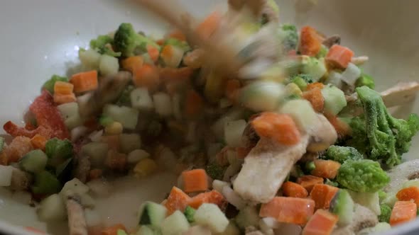 Cooking and mixing frozen vegetables in a white frying pan, making healthy vegetarian food, steam co