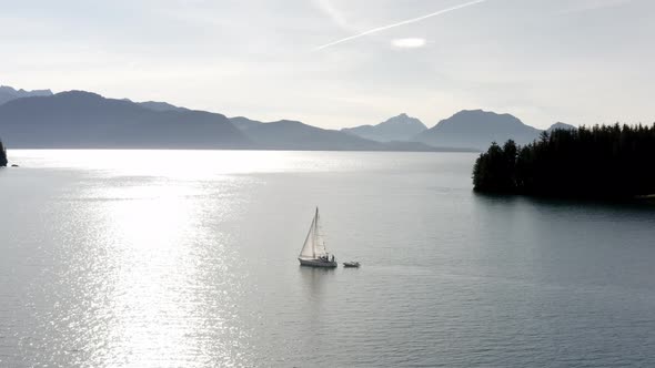 Small Boat Next To Luxury Yacht Sailing On Calm Ocean Water Illuminated By Sunlight With Mountain Si