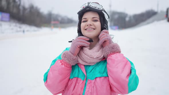 Portrait of Happy Young Woman with Toothy Smile Looking at Camera Adjusting Ski Helmet on Head