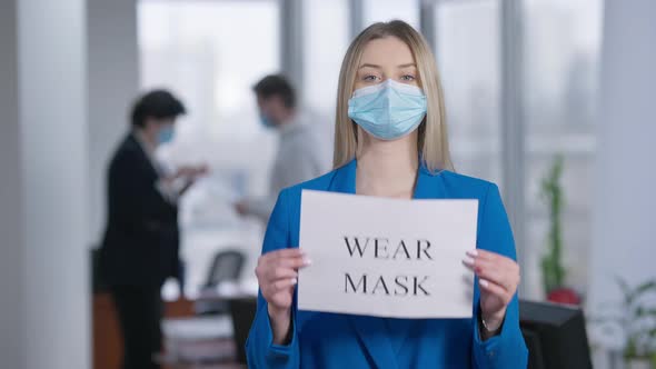 Middle Shot Portrait of Serious Young Blond Woman in Coronavirus Face Mask Raising Sign Wear Mask