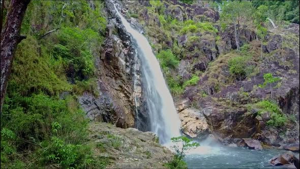 Drone Flies Over Waterfall Lake Rocks with Tree on Foreground