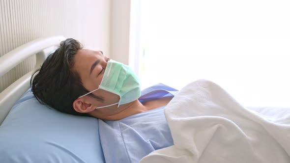 Unwell young Asian male patient lying down on hospital bed recovery after fell ill with cold and flu