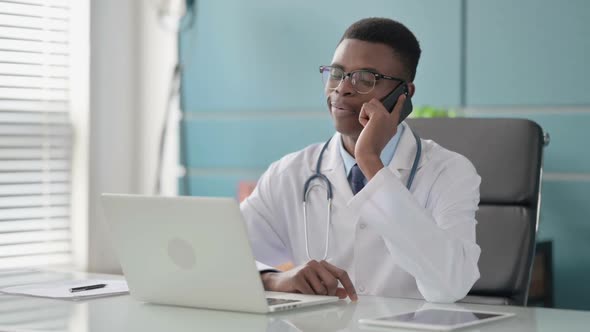 Young African Doctor Talking on Phone While Using Laptop in Office