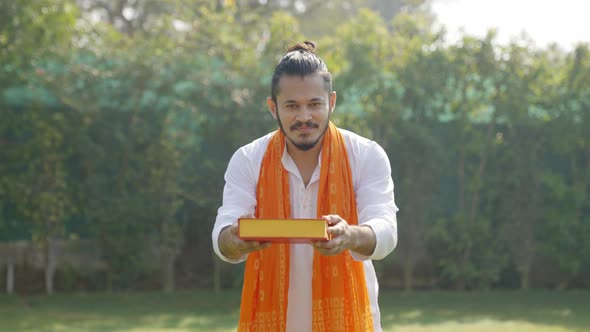 Indian man offering sweet box to the camera in an Indian traditional outfit Kurta Pajama