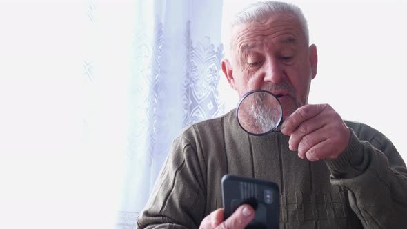 An Old Grayhaired Man Looks Through Social Networks Using a Smartphone