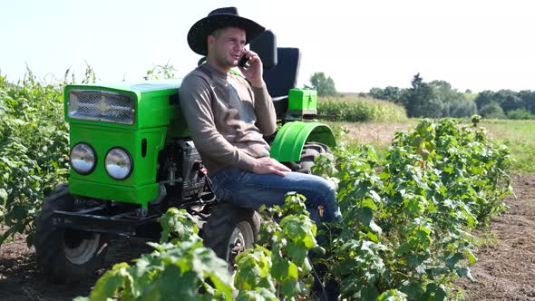 A Young Farmer Uses a Smartphone He is Resting Near His Tractor