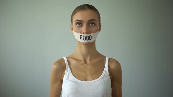 Skinny Girl With Taped Mouth Showing Empty Plate, Concept of Hunger and Anorexia