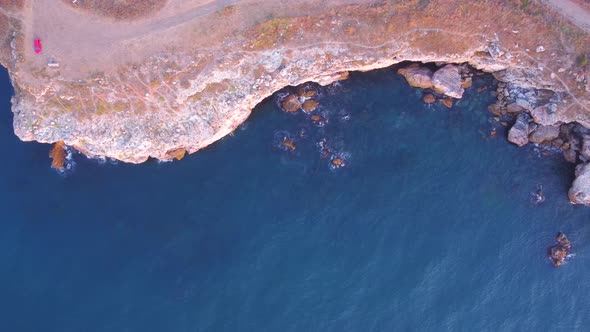 Top down aerial view of waves splash against rocky seashore, background. Flight over high cliffs of