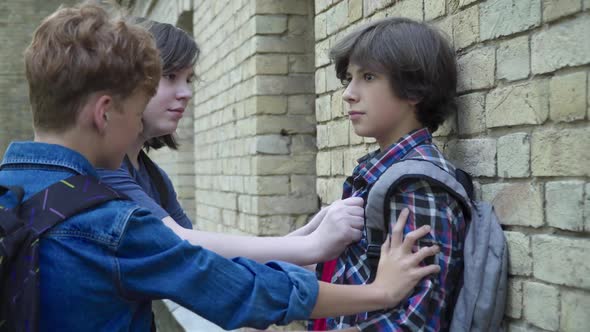 Side View of Aggressive Boys Pushing Scared Victim To Wall on Schoolyard. Rude Caucasian Classmates