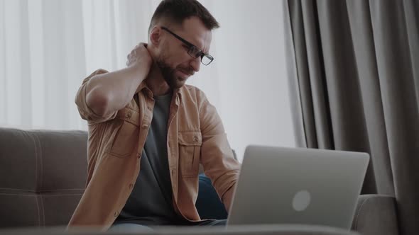 Millennial Man Sitting on Couch Touching Massaging Neck