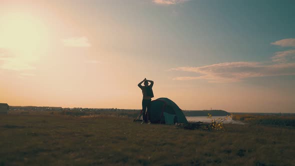 Man Silhouette Comes To Bonfire From Tent in Camp at Sunrise