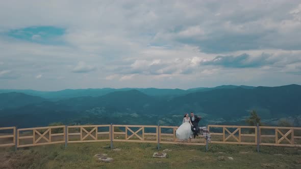 Groom with Bride Sit on the Fence Near Mountain Hills. Aerial Drone Shot