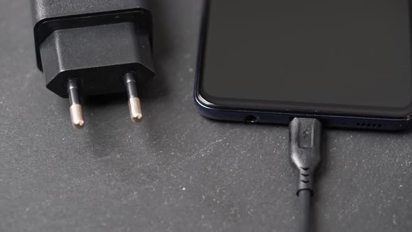 Rotating Closeup of Charger Plugged Into Turned Off Smartphone on Grey Surface