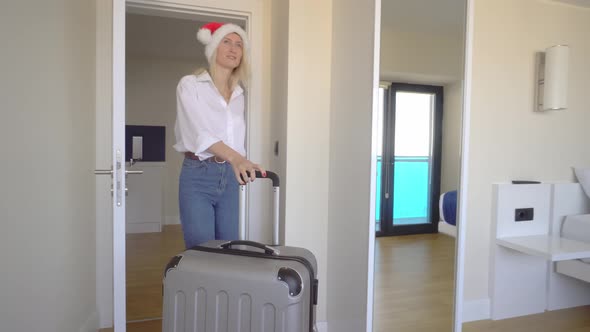 woman in a Santa Claus hat enters the hotel with a suitcase and goes to window.