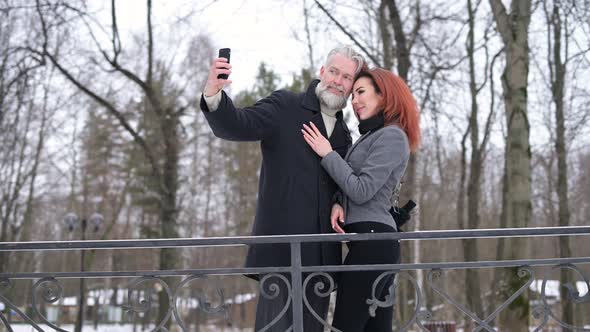 A gray-haired man and a young woman take a selfie while walking in the park