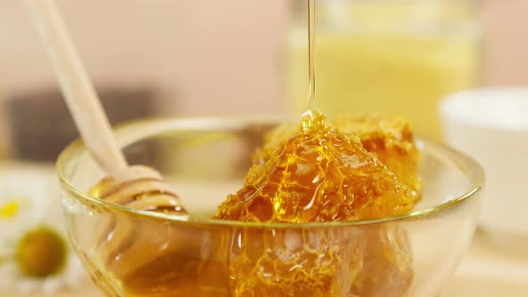 Sweet Honey Flowing on Honeycomb in Bowl with Wooden Spoon Closeup