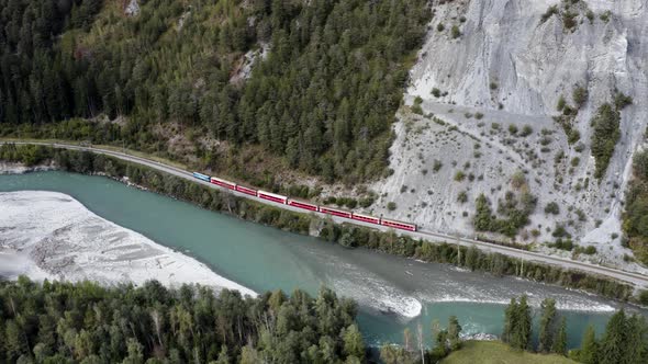 Red train drives in the scenic rhine canyon in Switzerland, aerial view.