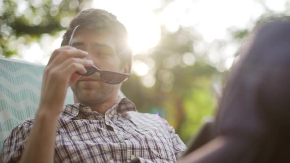 Young Caucasian Male Sitting in Park on Lounge Wearing Plaid Shirt and Sunglasses in Slowmotion