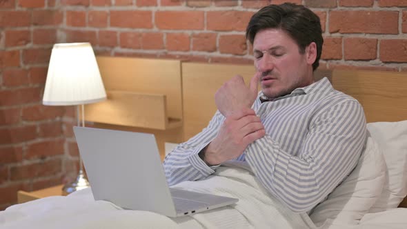 Middle Aged Man having Wrist Pain, Working on Laptop in Bed