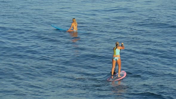 A young woman SUP surfing in a bikini on a stand-up paddleboard surfboard.