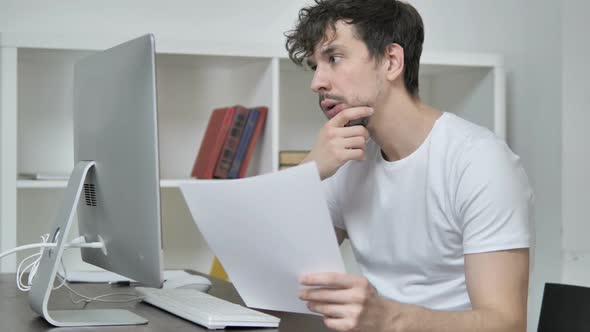 Pensive Young Creative Man Reading Documents Brainstorming at Work alt