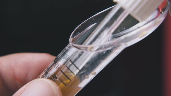 Man Takes Liquid From Spoon with Pipette on Dark Background