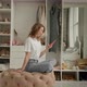 the Girl Sits on an Ottoman in the Dressing Room and Looks at the Phone - VideoHive Item for Sale