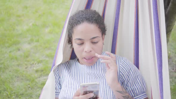 Portrait of Adorable Young African American Woman Lying in the Hammock, Relaxing in the Garden