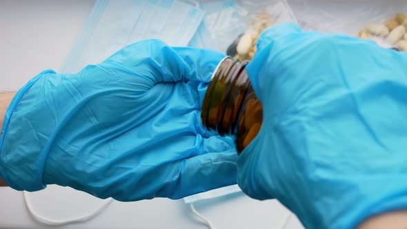 A Doctor Wearing Blue Gloves Pours a Large Quantity of White Pills From a Bottle Into His Hand