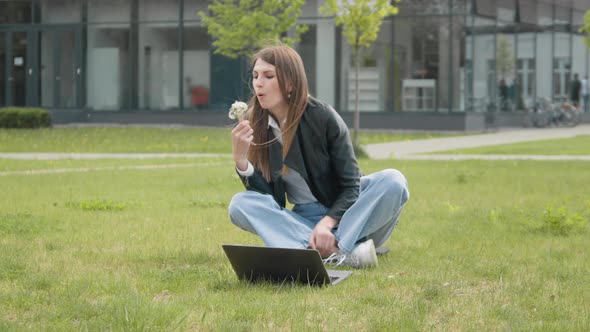Young Stylishly Dressed Girl Sitting in the Park on the Grass Near the Computer