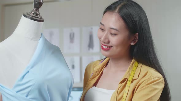 Smiling Asian Female Designer Wearing Fabric On A Mannequin While Designing Clothes In The Studio