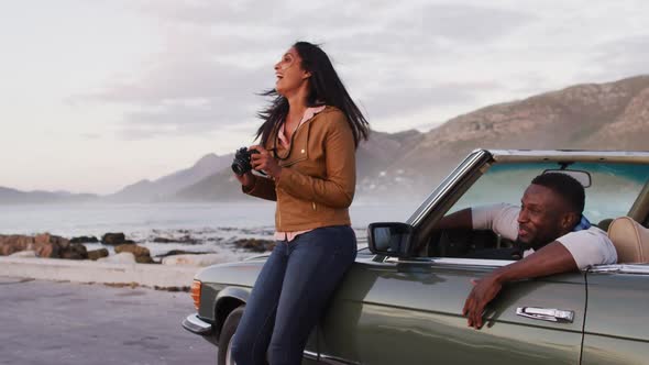 African american woman using digital camera to take pictures while standing near the convertible car