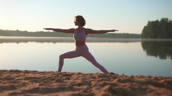 Healthy woman practicing yoga exercises on the beach in the morning at sunrise. Slow motion.