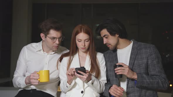 Young Employees in Business Clothes Are Standing in the Office Discussing Ideas Using a Smartphone