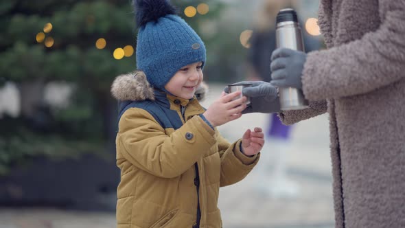 Portrait of Cute Middle Eastern Boy Standing at Christmas Tree in City with Unrecognizable Woman