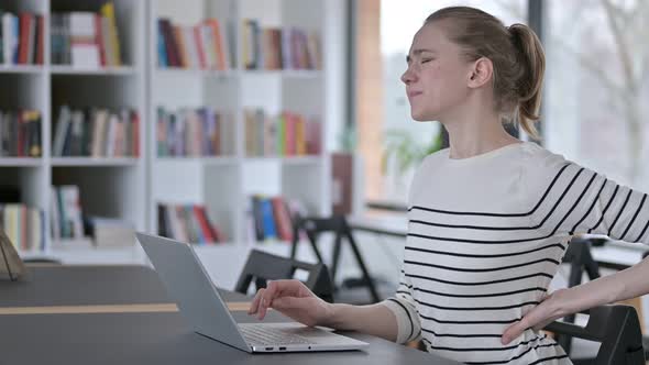 Young Woman with Back Pain Using Laptop in Library 